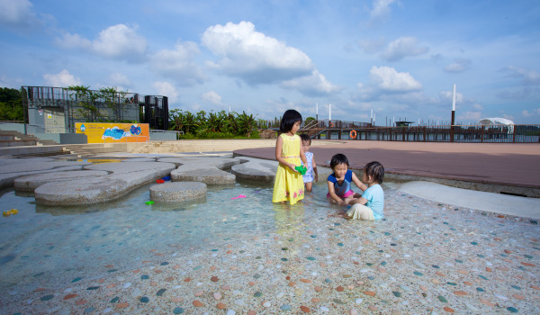 Four children play in a shallow water feature on a sunny day.